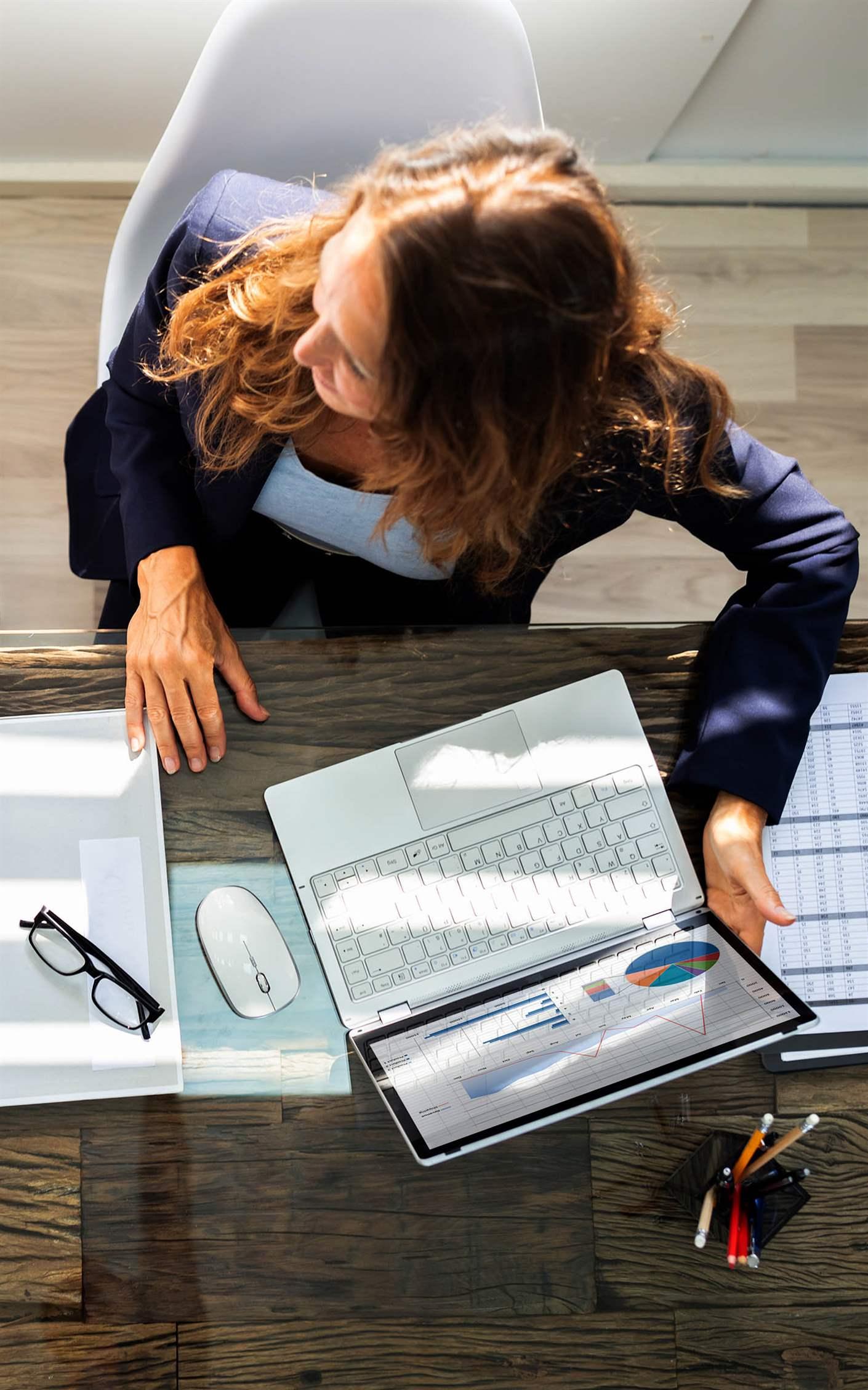 An Overhead View Of Two Businesspeople Calculating Invoice In Office While Using Laptop